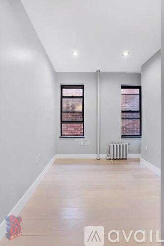 A spacious room with two windows and a radiator on the floor.