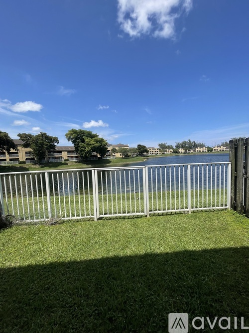 A fenced grassy area with a body of water and buildings in the distance.