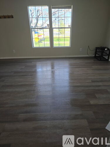 A room with wooden flooring and a window showing a view of a car and trees.