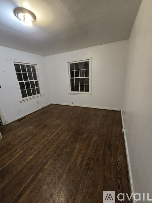 A room with wooden flooring and two windows.