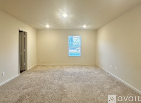 A spacious room with a carpeted floor and a window with blinds.