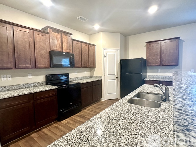 A kitchen with brown cabinets and a black fridge.