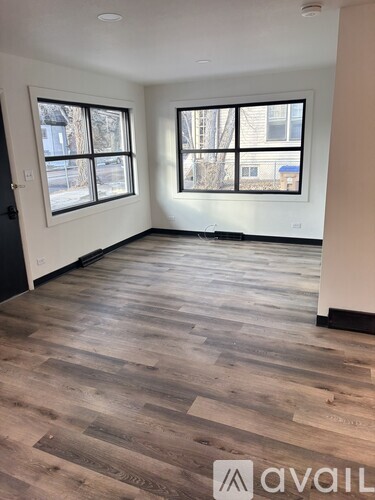 A room with wooden flooring and two windows.