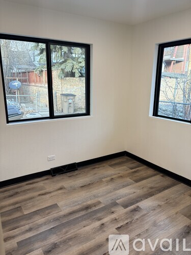 A room with wooden flooring and two windows.
