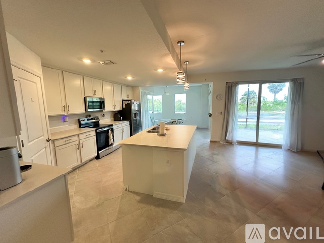 A kitchen with white cabinets and appliances, a large island, and a sliding glass door leading to a balcony.