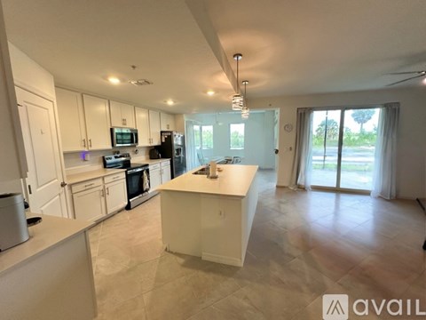 A kitchen with white cabinets and appliances, a large island, and a sliding glass door leading to a balcony.