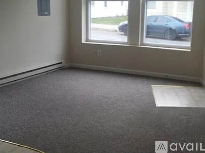 A room with a grey carpet and a window overlooking a street.