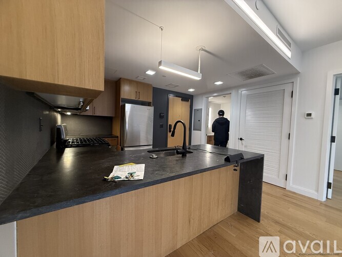 A man stands in a kitchen with a black countertop and wooden cabinets.