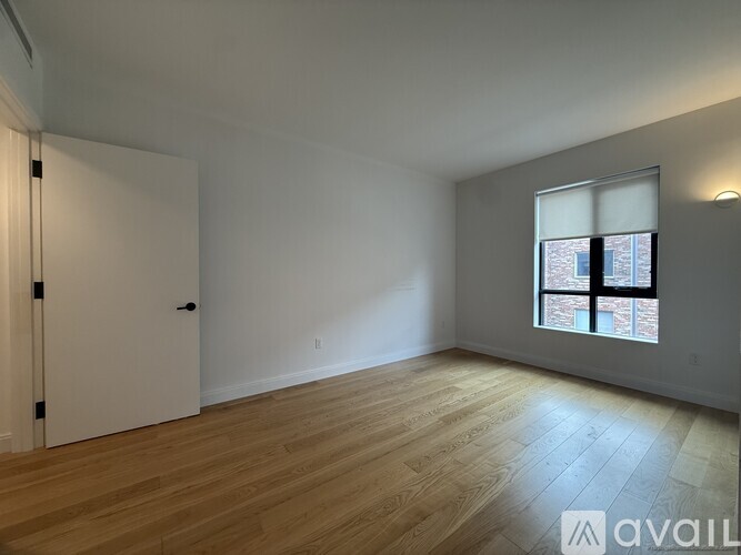 A room with wooden flooring and a window showing a brick building outside.