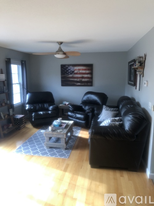 A living room with black leather furniture and a ceiling fan.