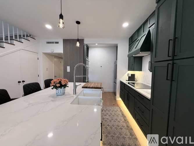 A modern kitchen with a marble table and dark green cabinets.