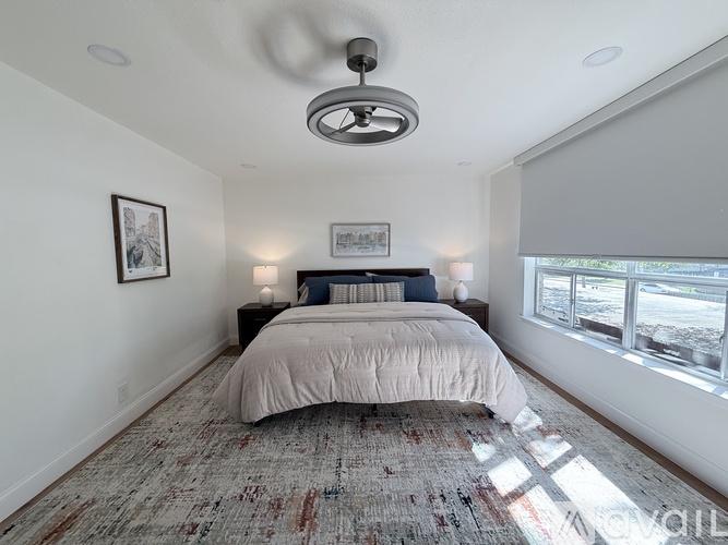 A bedroom with a bed, a ceiling fan, and two wall lamps.