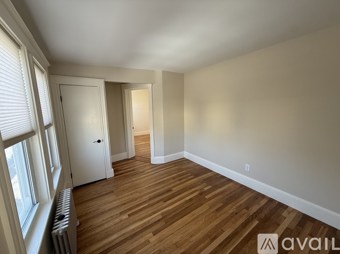 A room with wooden floors and white walls, with a door and a window.