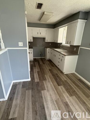A kitchen with wood flooring and white cabinets.