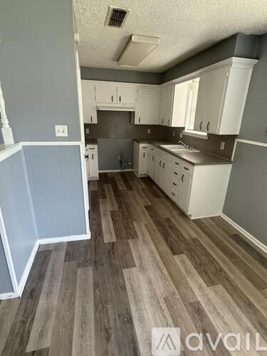 A kitchen with wood flooring and white cabinets.