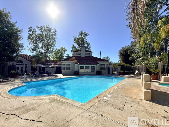 A sunny day at a pool with a house in the background.