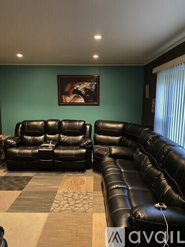 A living room with black leather couches and a painting on the wall.