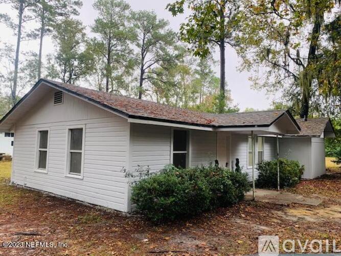 A small white house with a brown roof is surrounded by trees.