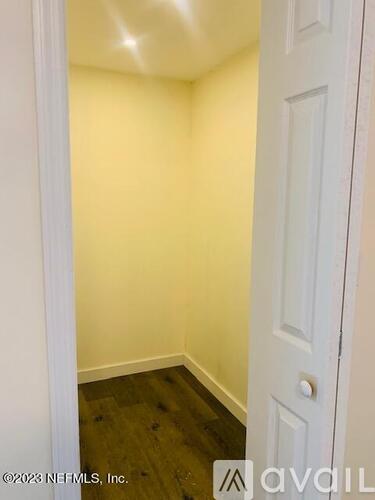 A white door is on the right side of a room with a wooden floor.