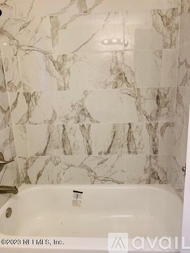 A bathroom with a marble tile wall and a white bathtub.