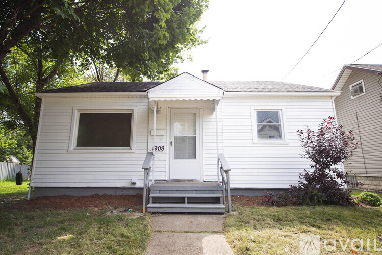 A small white house with a porch and a tree in front.