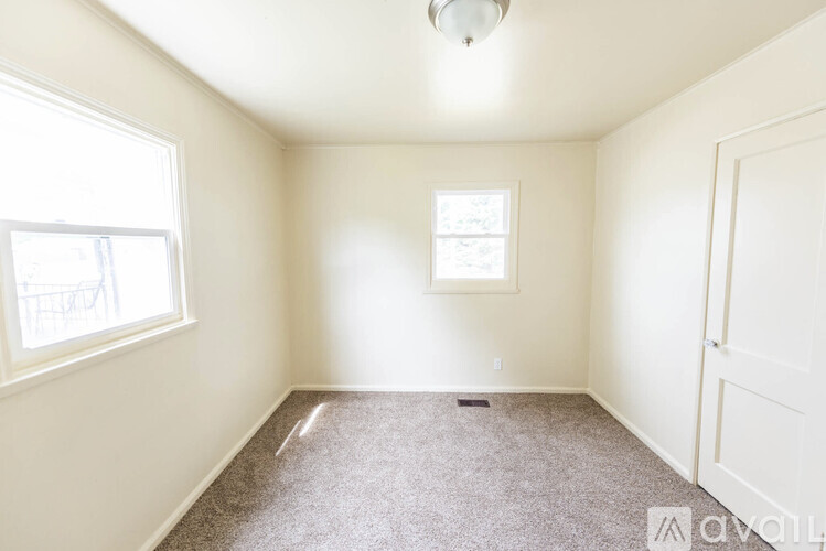 A room with a carpeted floor, a ceiling light, and a window with a view of a balcony.