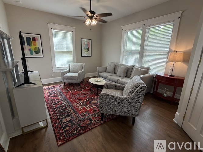 A living room with a grey sofa, a grey armchair, a red rug, and a ceiling fan.