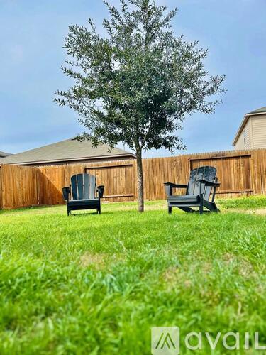 Two black chairs are placed on a lawn in front of a wooden fence.