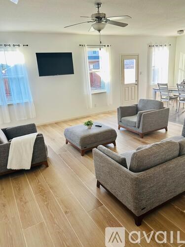 A living room with a grey sofa, ottoman, and a television on the wall.