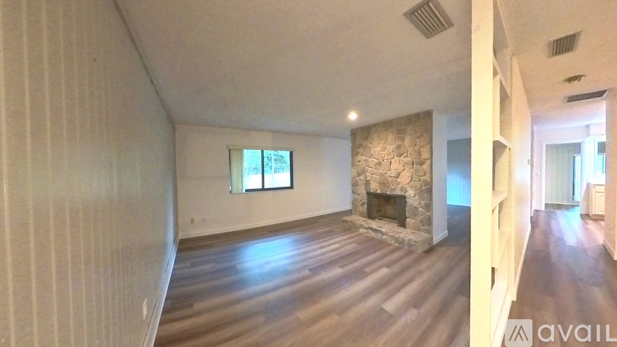 A spacious living room with a stone fireplace and wood flooring.