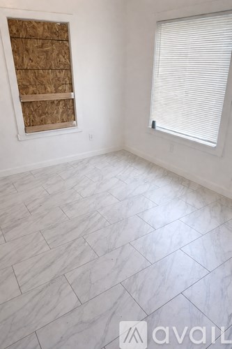 A room with a window covered in blinds and a wall with a window covered in plywood.