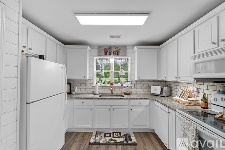 A kitchen with white cabinets and appliances, a window with a view of a garden, and a rug on the floor.