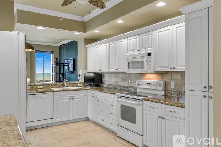 A kitchen with white cabinets and appliances, a ceiling fan, and a window with a view of the ocean.