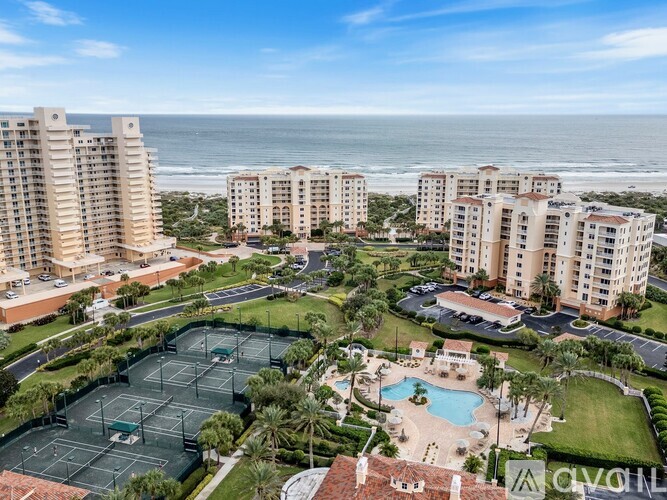 A view of a resort with a tennis court, swimming pool, and beach in the background.