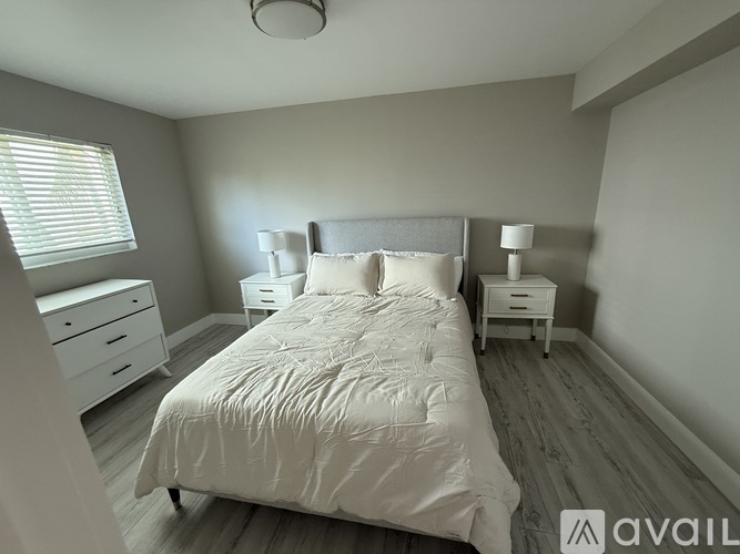 A bedroom with a large bed, two nightstands, and a window with blinds.