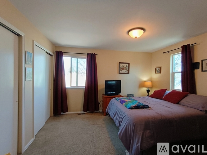 A bedroom with a bed, a television, and a window with curtains.