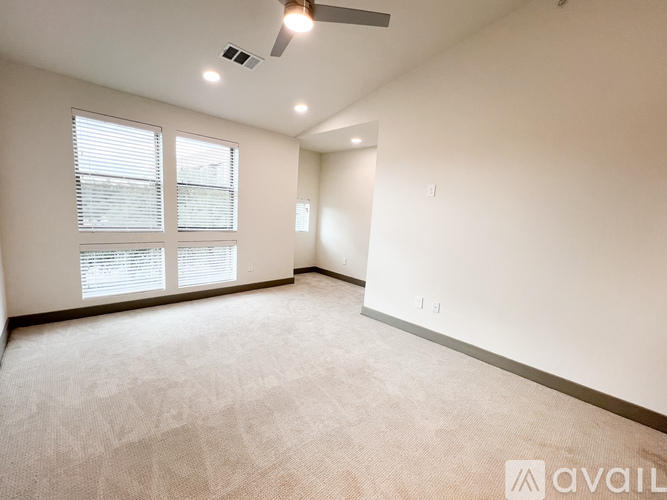 A spacious room with a carpeted floor, a window with blinds, and a ceiling fan.