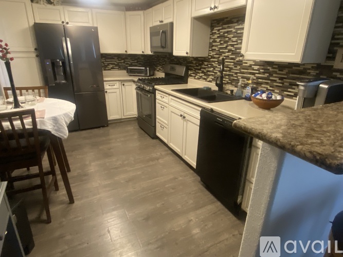 A kitchen with a table and chairs in the foreground and a refrigerator, oven, and microwave in the background.