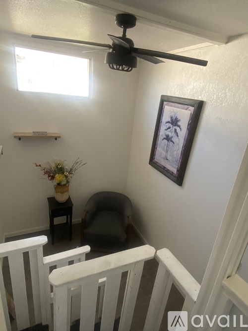 A room with a ceiling fan and a picture of palm trees on the wall.