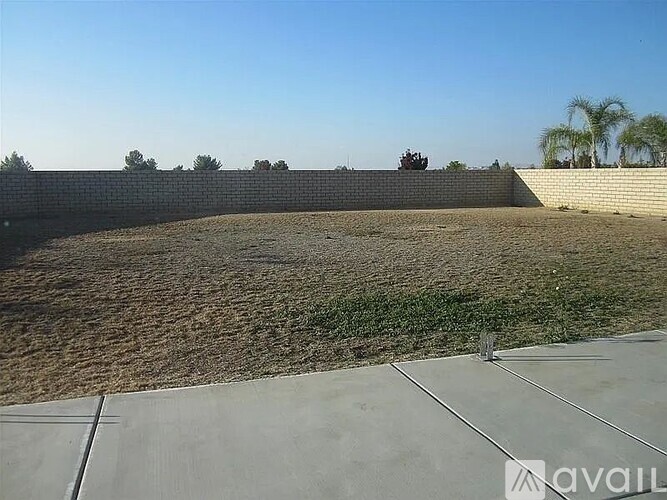 A large, empty, sandy yard with a wall and a concrete path.