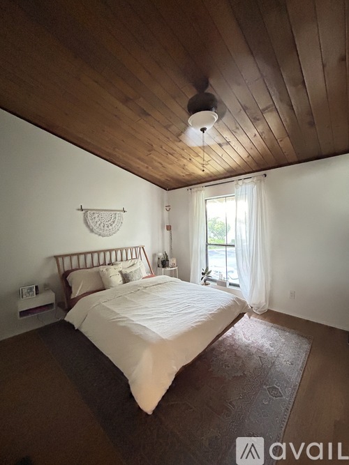 A bedroom with a bed, a wall hanging, and a window.