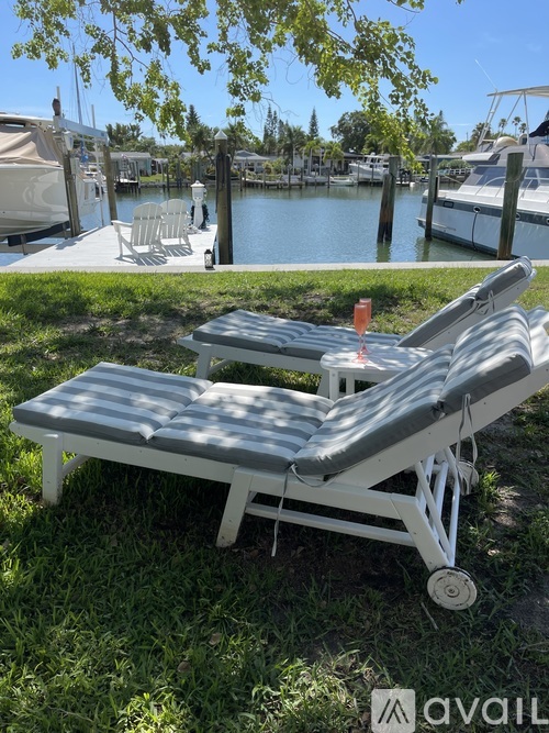 A white folding bed with a grey mattress is on a grassy area near a body of water.