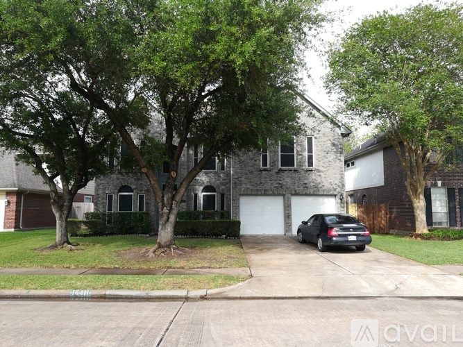 A black car is parked in front of a grey house with a white garage door.