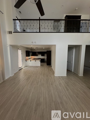 A spacious room with wooden flooring and a balcony with a railing.