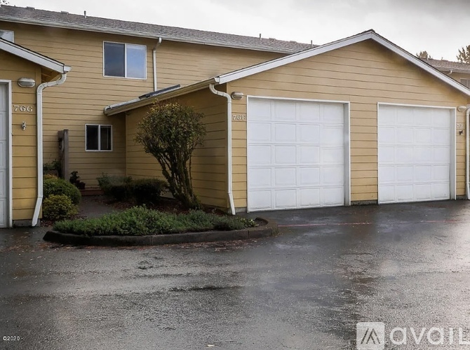 A beige house with two garages and a tree in front.