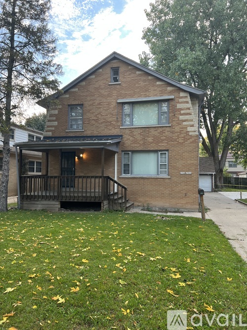 A brick house with a porch and a tree in front.
