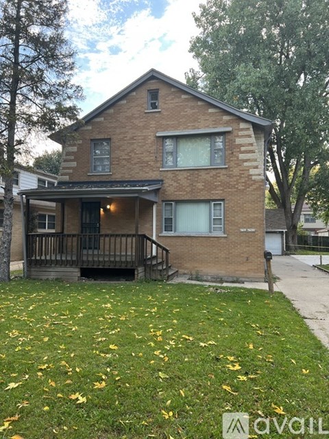 A brick house with a porch and a tree in front.