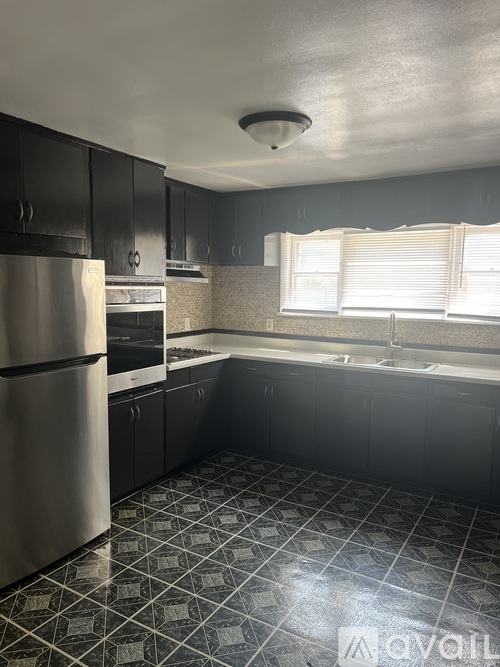 A kitchen with a stainless steel refrigerator and black cabinets.