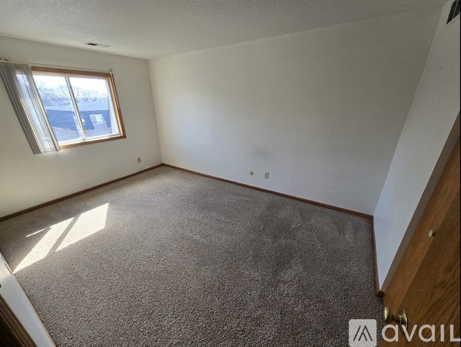 A carpeted room with a window and wooden trim.