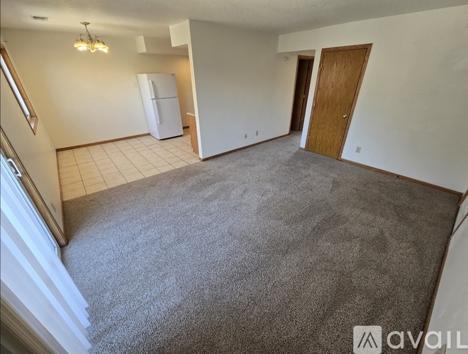 A spacious living room with a carpeted floor and a white refrigerator in the corner.